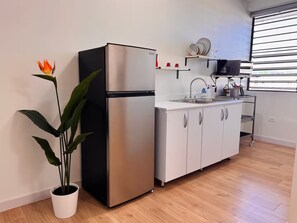 Una cucina moderna con frigorifero in acciaio inossidabile, mobili bianchi, un lavello e una pianta in vaso.