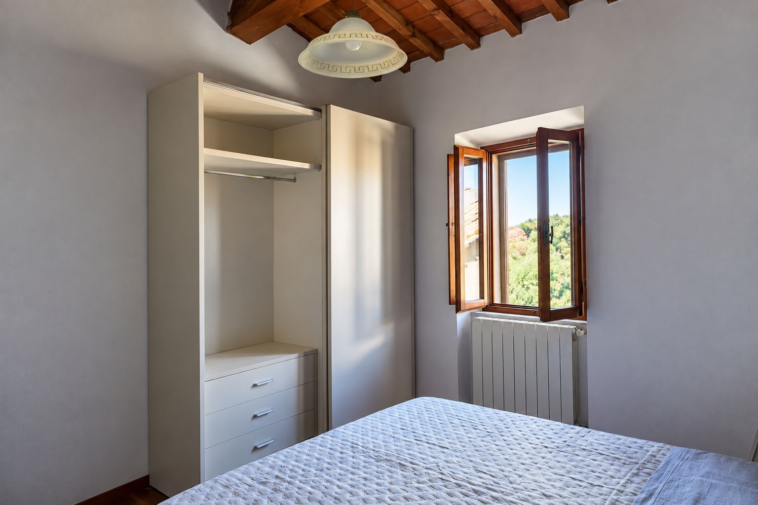 A bedroom with a bed, a wardrobe, a window with a view, and a radiator.