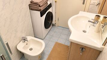 Une petite salle de bain équipée d’un lave-linge, d’un bidet et d’un lavabo.