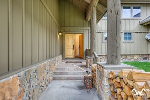 A stone staircase leading to a wooden door, with a firewood stack and a bench on the right. - Howling Elk Hideaway (Big Sky)