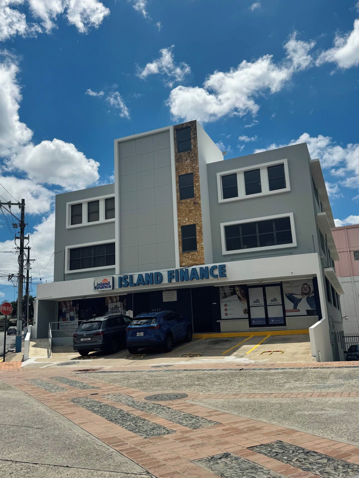 A modern building with a sign reading 'Island Finance' and two parked cars in front.