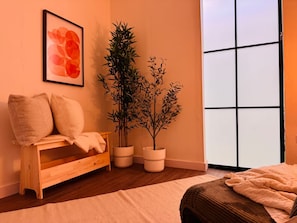 A room with a wooden bench, a potted plant, a framed artwork, and a large window.