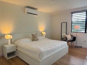 Een moderne slaapkamer met een groot bed, bedlampjes, een staande lamp, een stoel en een raam met jaloezieën.