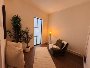 A room with a sofa, a floor lamp, a potted plant, and a window.