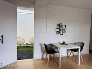 A modern dining area with a white table and black chairs, a small potted plant, and a wall-mounted picture frame.