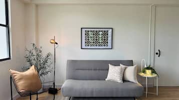 Una sala de estar moderna con un sofá gris, una lámpara de pie, una obra de arte enmarcada y una planta en maceta.