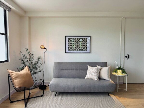 A modern living room with a grey sofa, a floor lamp, a framed artwork, and a potted plant.