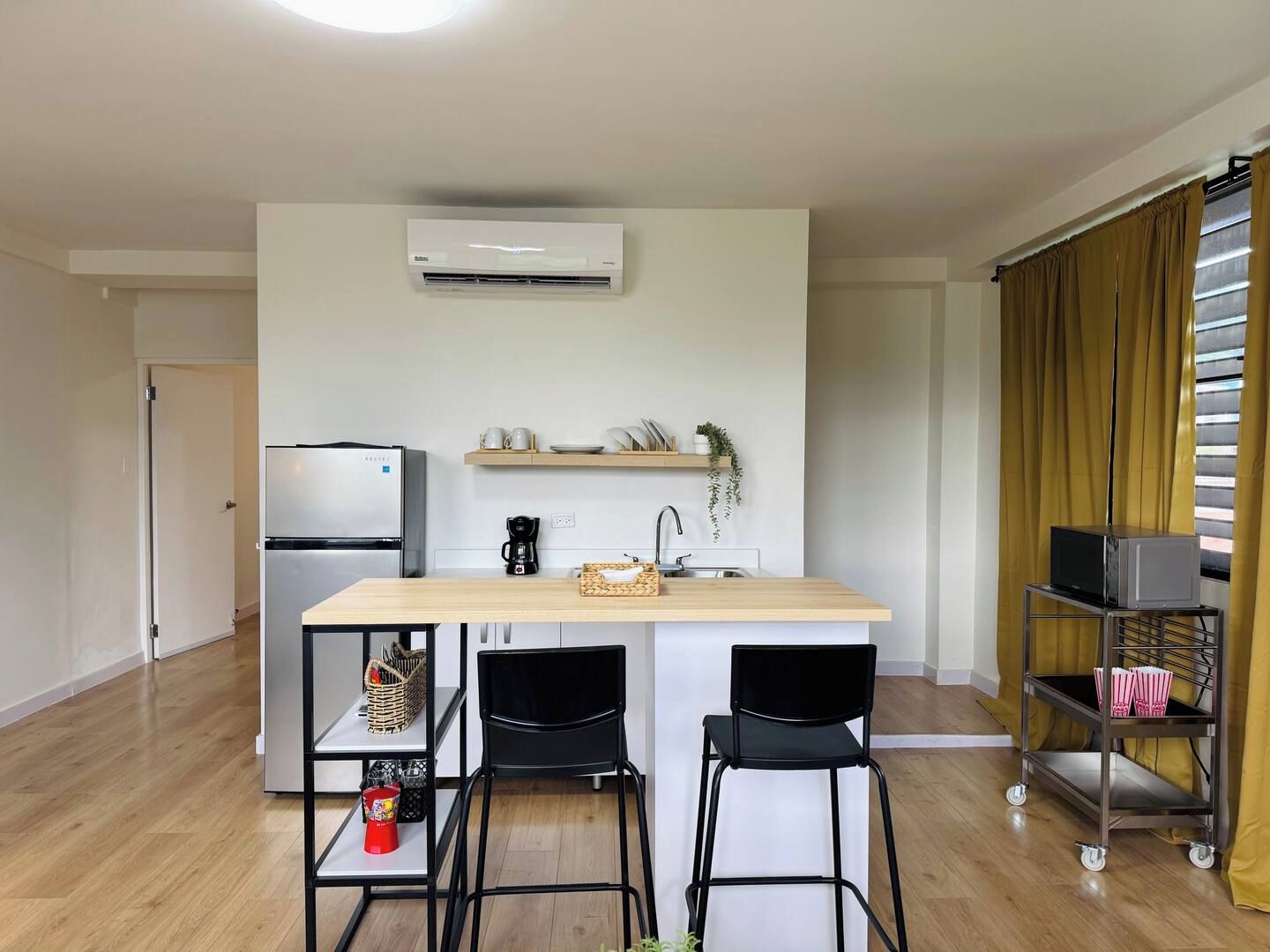 A compact kitchen with a refrigerator, a coffee maker, and a microwave on a shelf. There are two chairs and a small table in the center.