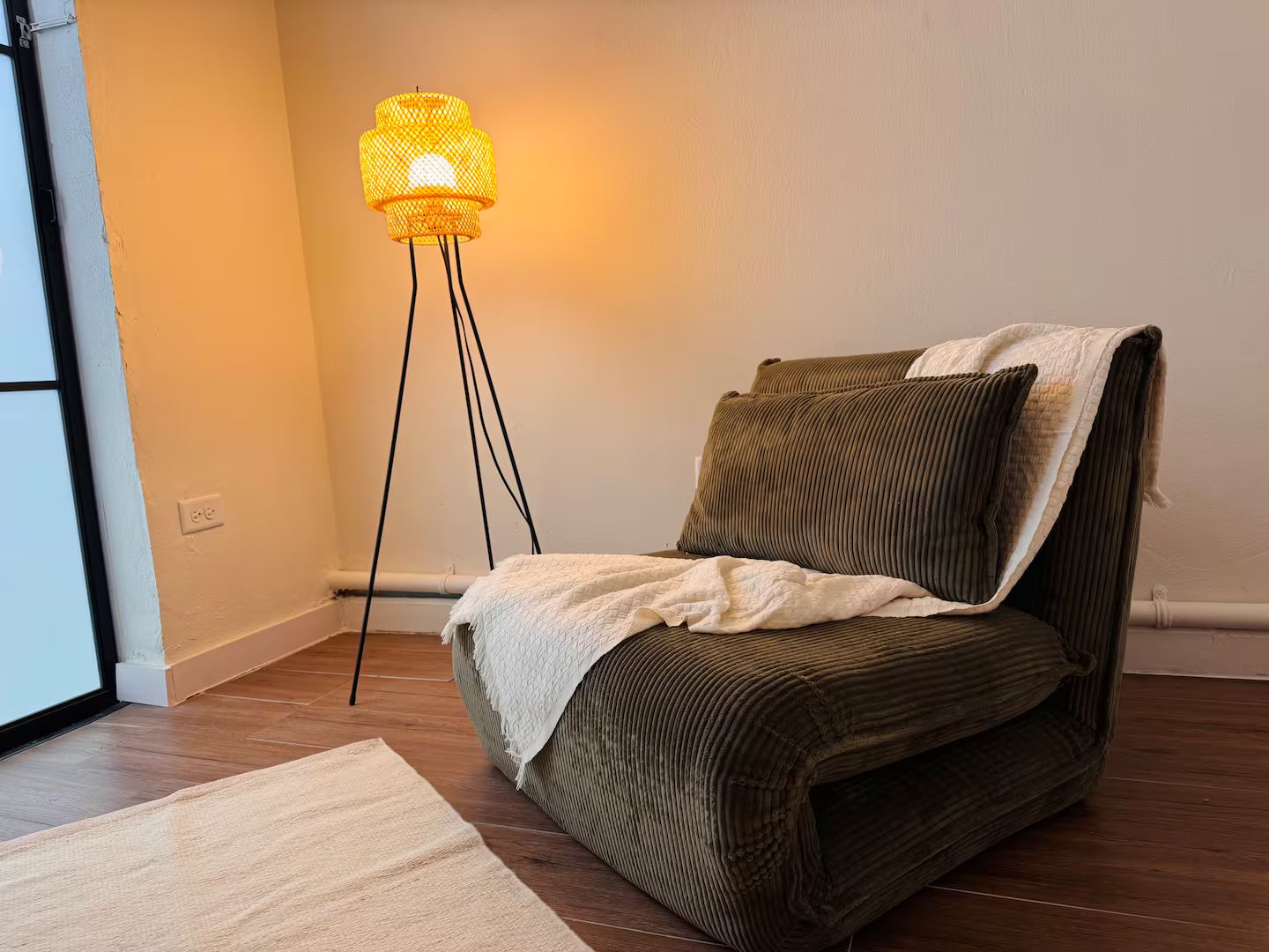 Une pièce avec un seul canapé marron, un plaid blanc et un lampadaire avec un abat-jour jaune.