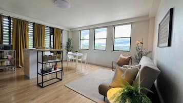 Amplia sala de estar con sofá, mesa de comedor y zona de cocina con refrigerador y estanterías.