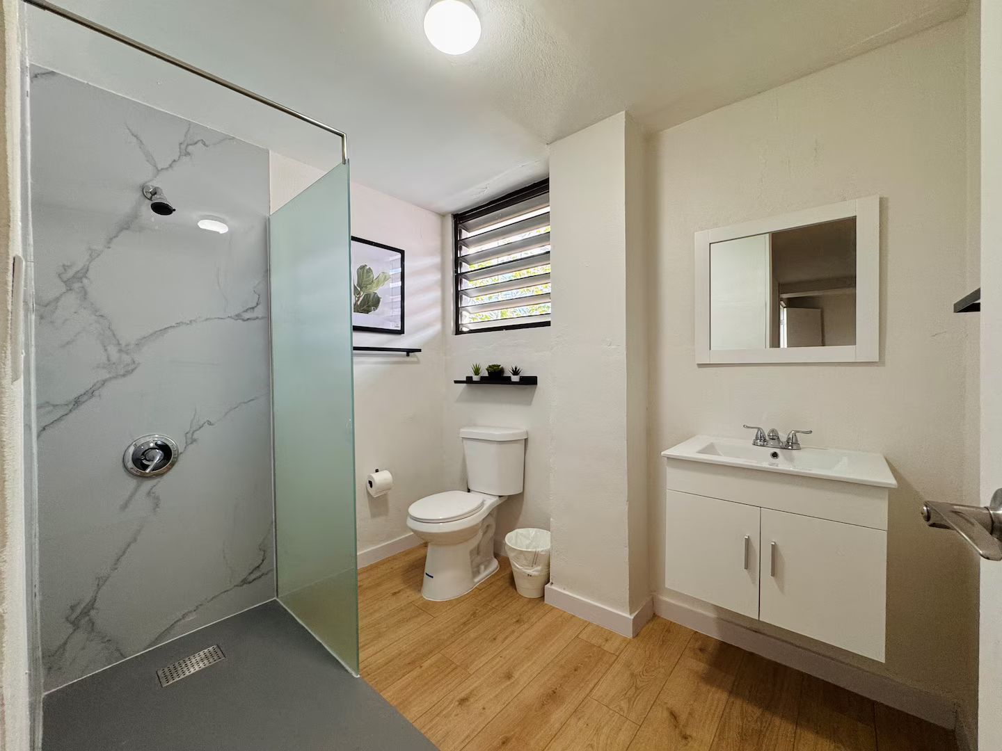 A bathroom with a shower, toilet, sink, and mirror.