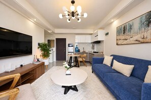 Ein modernes Wohnzimmer mit einem Flachbildfernseher, einem blauen Sofa, einem runden Couchtisch und einem Essbereich mit einem weißen Tisch und Stühlen.