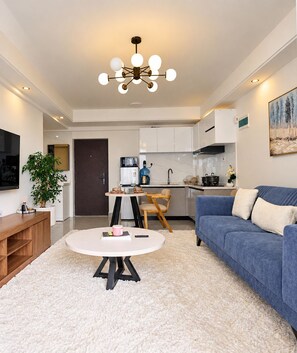 Ein modernes Wohnzimmer mit einem blauen Sofa, einem runden Couchtisch und einem Fernseher auf einem Holzgestell.