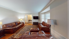 A living room with a brown leather sofa set, a flat-screen TV mounted on the wall, and a patterned rug on the floor.