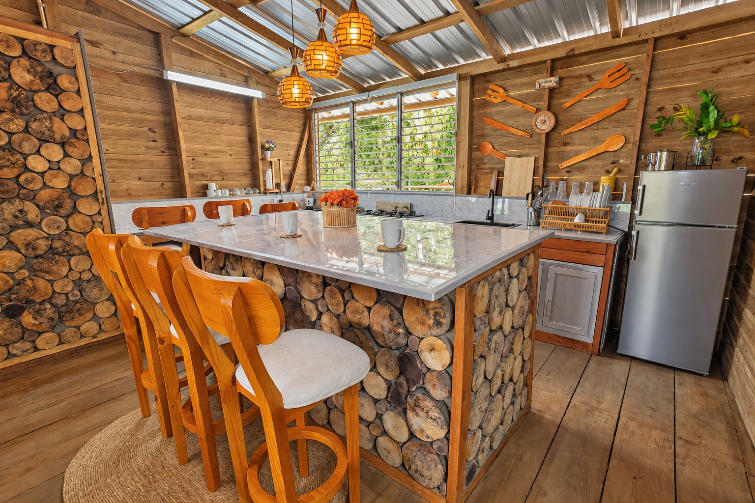Una cocina con una isla central, sillas de madera, un refrigerador y una lámpara colgante.