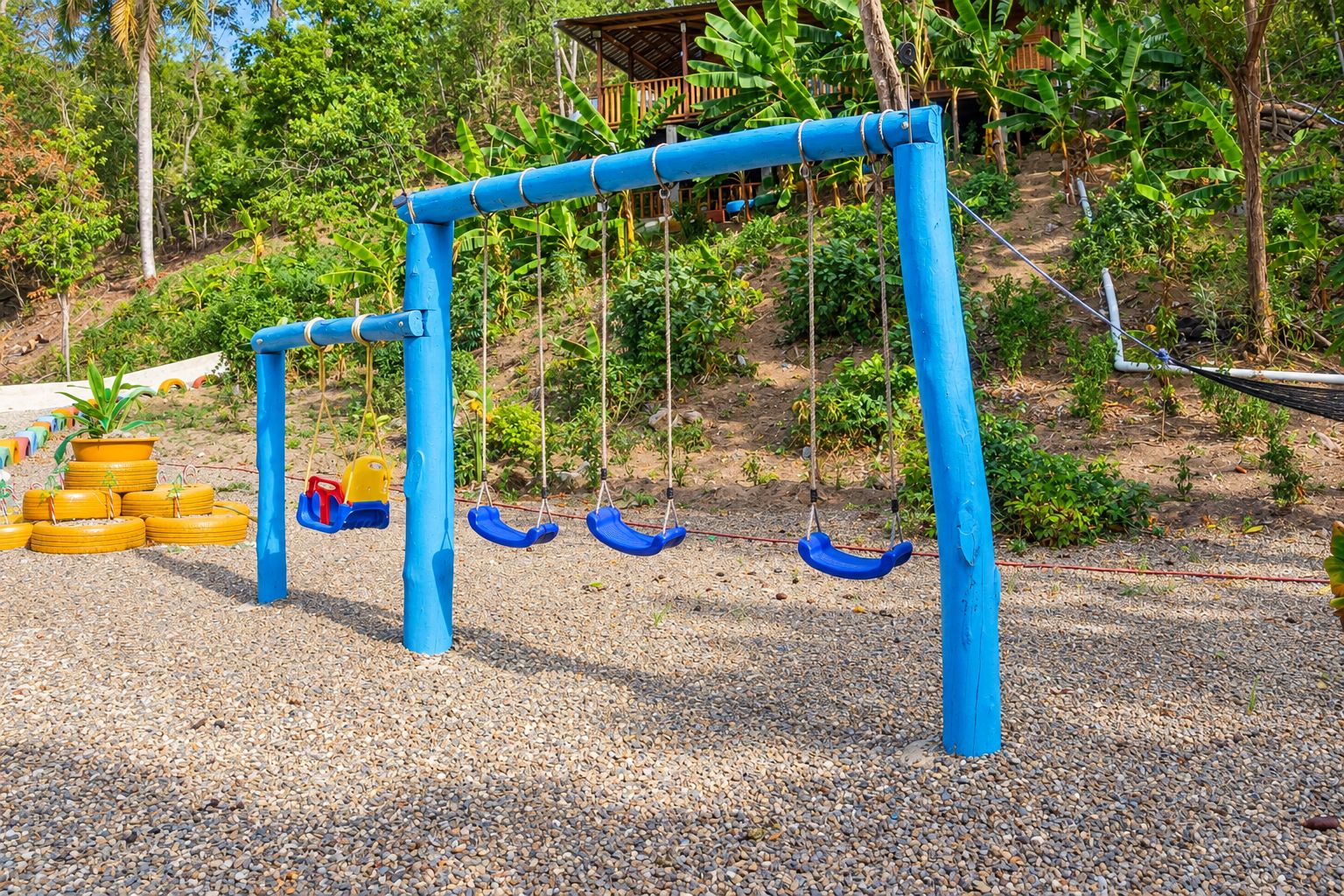 A playground with swings and tire swings, surrounded by greenery.