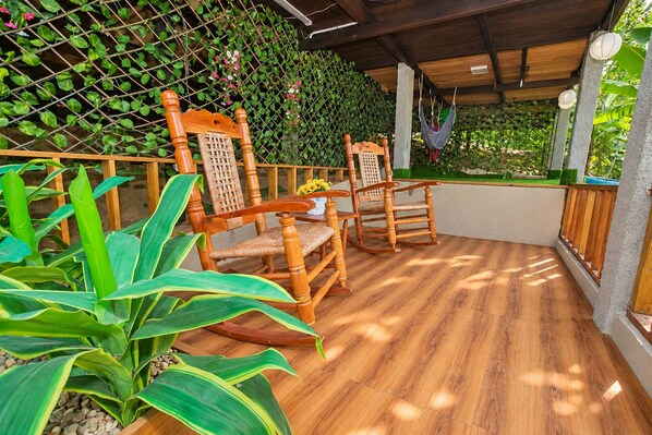 A wooden deck with two rocking chairs and a table, surrounded by lush greenery and a wooden fence. - Tropical villa with a pool, bar, and sunsets (El Puerto)