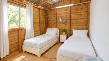 A bedroom with two beds, wooden walls, a ceiling with metal beams, a bedside table with a plant, and a window with curtains.
