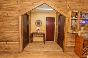 Un interior de madera con una puerta central, una mesita con un florero y una zona de bar con botellas y vasos.