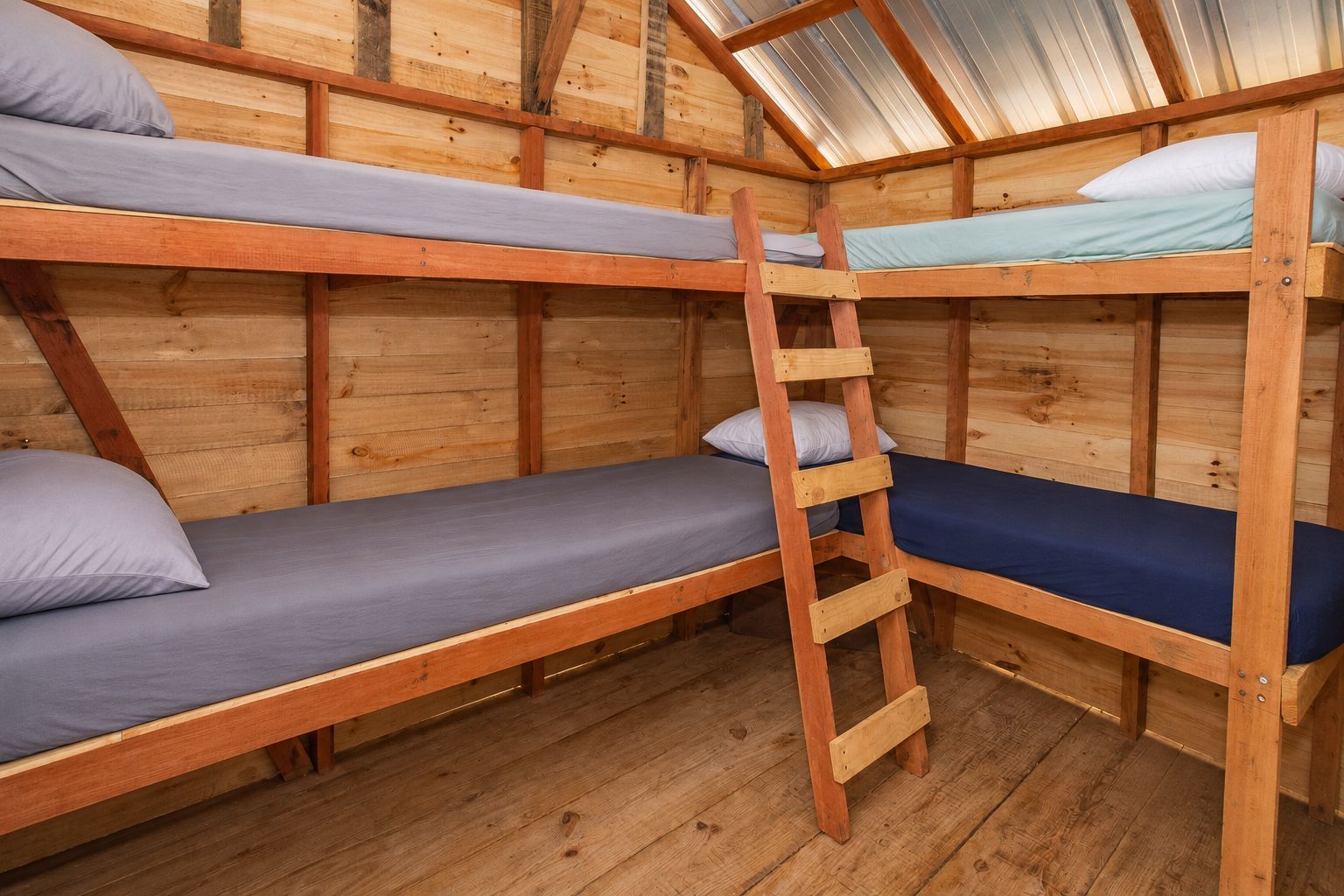 Habitación con literas de madera, escalera, paredes de madera y techo inclinado.