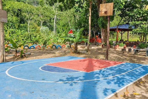 Un terrain de basket en plein air, entouré de verdure et d’arbres.