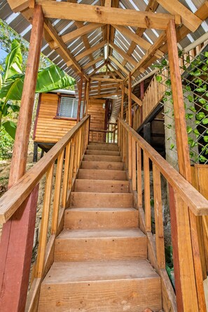 A wooden staircase leading to a covered area with a metal roof, surrounded by greenery. - Tropical villa with a pool, bar, and sunsets (El Puerto)