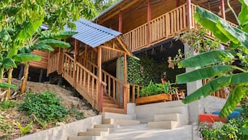 A wooden staircase leading to a covered porch with a metal roof, surrounded by lush greenery.