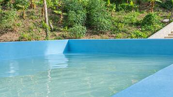 Piscina azul cristalina con borde de hormigón, rodeada de abundante vegetación.