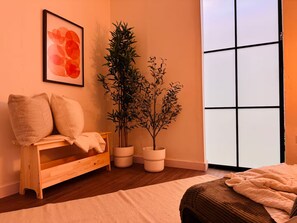Ein Zimmer mit einer hölzernen Bank, zwei Topfpflanzen, einem gerahmten Kunstwerk und einem großen Fenster.