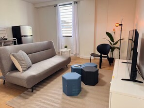 A modern living room with a sofa, ottomans, a television, and a potted plant. - Central San Germán - Private Patio / Generator (San Germán)
