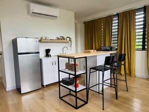 Een moderne keuken met een koelkast, koffiezetapparaat en een houten tafel met stoelen.