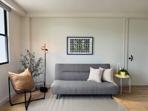 A modern living room with a grey sofa, a black metal chair, a floor lamp, and a framed abstract art piece on the wall. - Central Apt in Historic Town San German - King Bed (San Germán)
