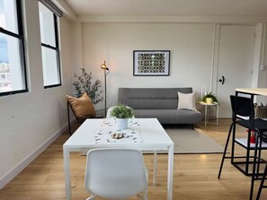 A modern living room with a white sofa, a dining table with chairs, a potted plant, and a framed artwork on the wall. - Central Apt in Historic Town San German - King Bed (San Germán)