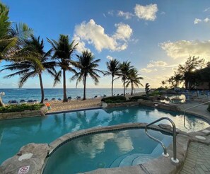 A pool with a view of the ocean, surrounded by palm trees and lounge chairs. - Oceanfront with Beautiful Views! @The Reef Resort in beautiful East End (East End)
