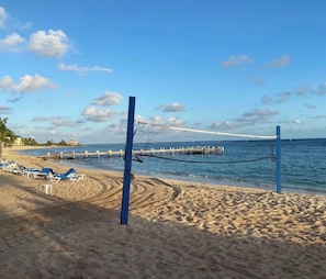 A beach volleyball net with blue poles, a sandy beach, and a calm sea. - Oceanfront with Beautiful Views! @The Reef Resort in beautiful East End (East End)