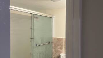 A bathroom with a glass-enclosed shower, a white toilet, and a beige tiled wall.