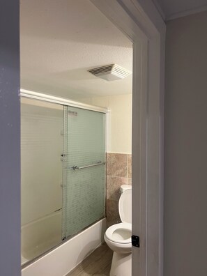 A bathroom with a glass-enclosed shower, a white toilet, and a beige tiled wall. - Tacoma GL (Tacoma)