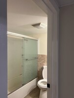 A bathroom with a glass-enclosed shower, a white toilet, and a beige tiled wall.