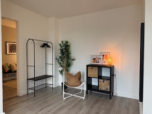 Quarto com uma cadeira branca, uma estante preta com cestos, um abajur e um vaso de planta.