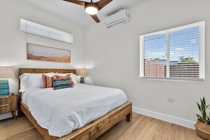A bedroom with a wooden bed, bedside lamps, a ceiling fan, an air conditioning unit, a window with blinds, and a wall-mounted air conditioner. - Vista Compound | Walk to Downtown/Shops/Dining (Vista)