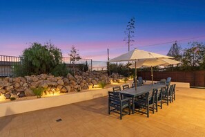 An outdoor patio with a stone wall, a table with chairs, and an umbrella. - Vista Compound | Walk to Downtown/Shops/Dining (Vista)