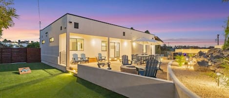 A modern two-story house with a patio area, outdoor seating, and a well-maintained lawn.