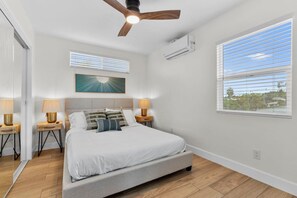 A bedroom with a bed, two bedside tables with lamps, a ceiling fan, an air conditioning unit, and a window with blinds. - Vista Hideaway | Food, Fun & Coastal Adventures (Vista)