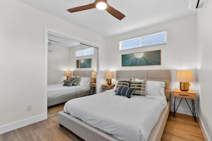 Ein Schlafzimmer mit zwei Betten, einem Deckenventilator, einem Fenster mit Jalousien und einem an der Wand hängenden Kunstwerk.