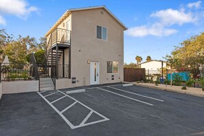 A two-story building with a parking lot in front, a staircase to the left, and a fenced area to the right. - Vista Hideaway | Food, Fun & Coastal Adventures (Vista)