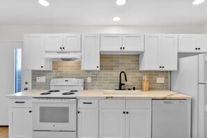 A modern kitchen with white cabinets, a white stove, a black faucet, and a tiled backsplash. - Vista Hideaway | Food, Fun & Coastal Adventures (Vista)
