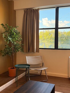 A room with a window, a potted plant, a chair, and a table. - Historic San Germán Retreat + Prime Location (San Germán)