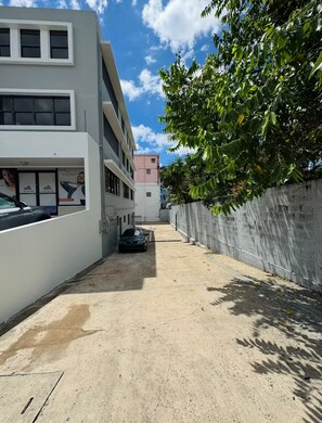 A narrow alleyway with a parked car, a white building with a window display, and a concrete wall on one side. - Historic San Germán Retreat + Prime Location (San Germán)