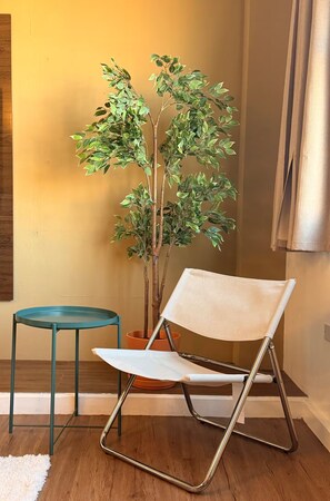 A room with a wooden floor, a green chair, a small table, and a potted plant. - Historic San Germán Retreat + Prime Location (San Germán)