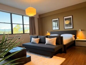 A modern bedroom with a large window, a sofa, a bed, and a hanging light fixture. - Historic San Germán Retreat + Prime Location (San Germán)